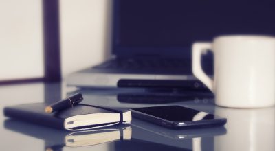 办公室场景中一名职场人士在午休时用手机查看视频资源索引，背景是整洁的办公桌和绿植